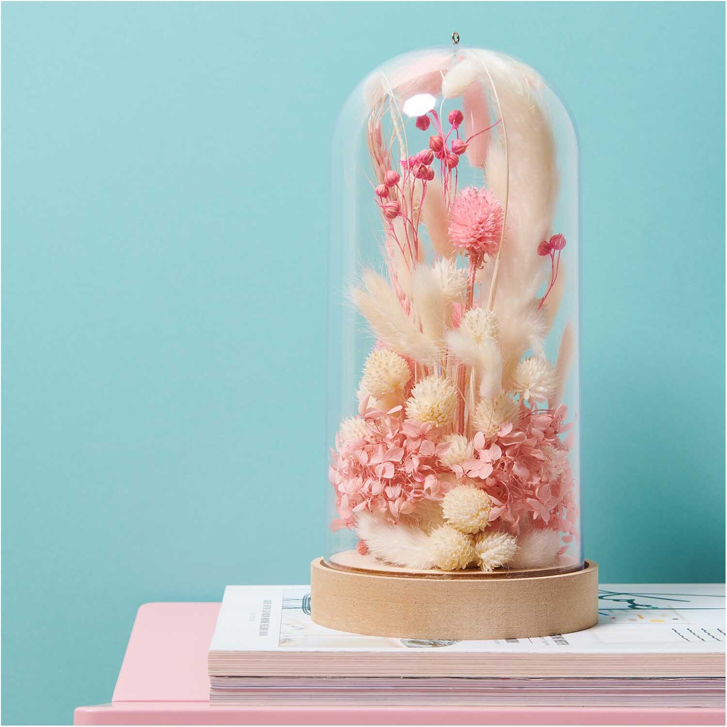 Getrocknete japanische Karde in einer Glasglocke auf einem Tisch, dekorativ arrangiert mit rosa und cremefarbenen Blüten von Rico Design.