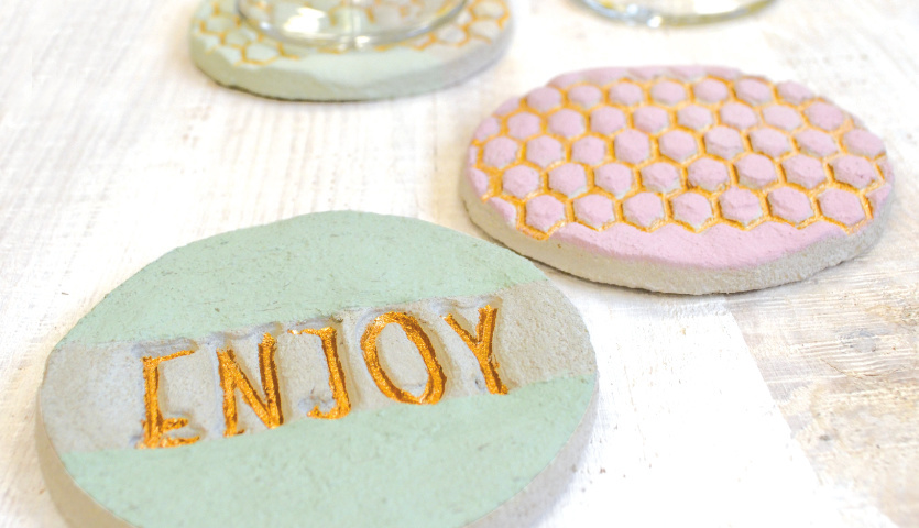 Bastelanleitung Glasuntersetzer aus Knetbeton: Runde Untersetzer in Pastellfarben mit Schriftzug und Wabenmuster auf hellem Holztisch.