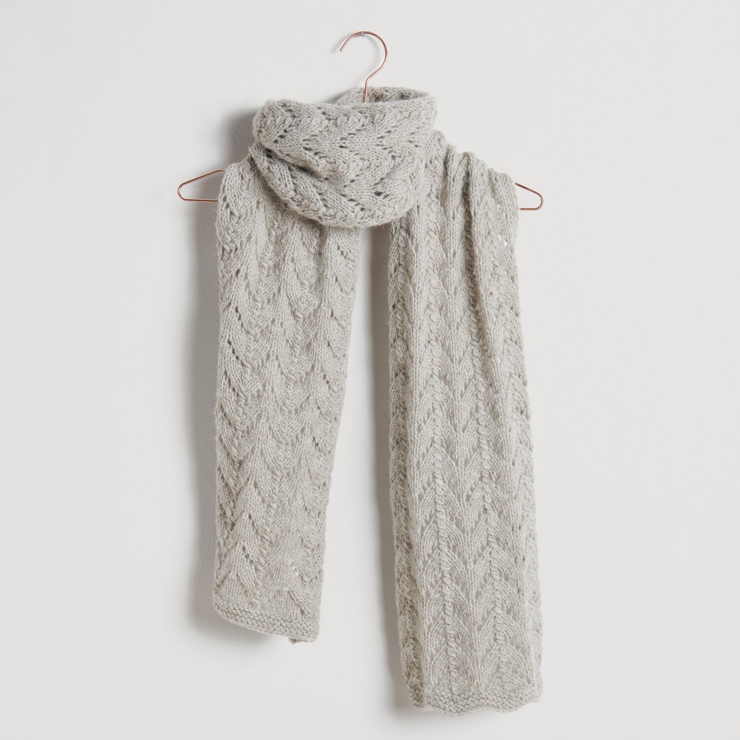 Strickset Schal Modell 09: Eleganter, hellgrauer Schal mit Zopfmuster, hängend an einem Kleiderbügel.