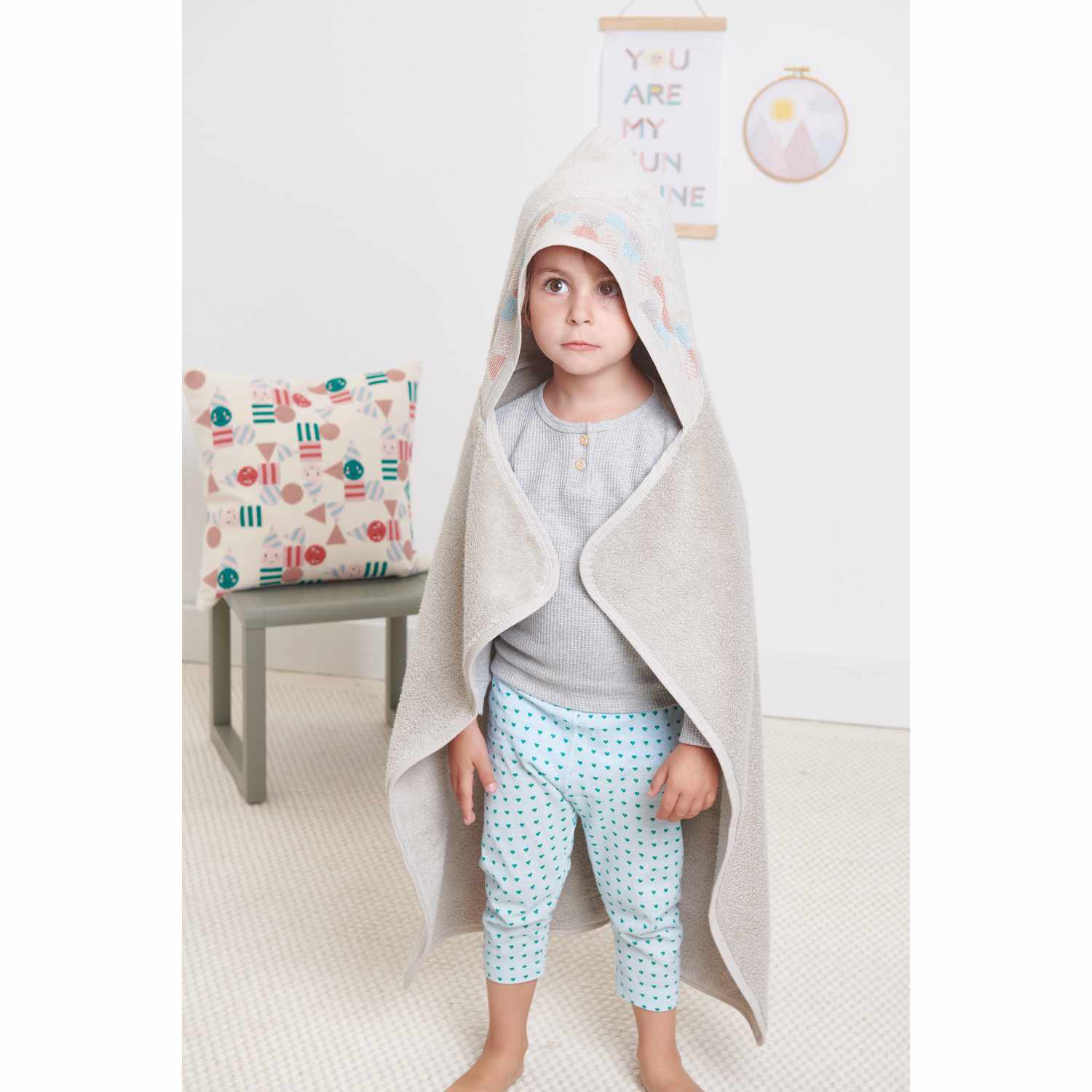 Jerseystoff Happy Baby Herzchen mint: Kind in mintfarbenem Herzchen-Outfit, umhüllt von einem Handtuch. Im Hintergrund ein dekoratives Kissen.