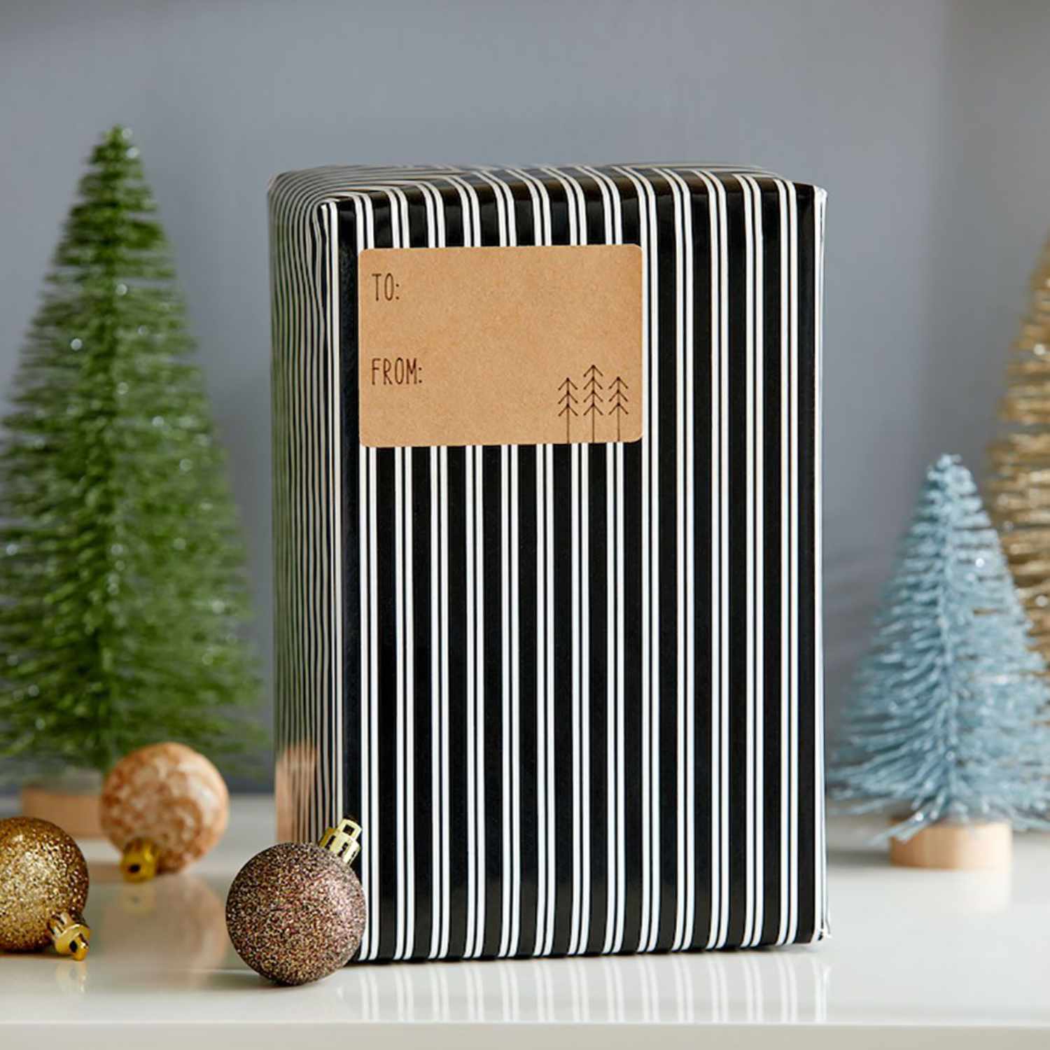 Joy Smart Label Cardstock auf Geschenk mit schwarz-weißem Streifenmuster, umgeben von Weihnachtsbäumen und Kugeln.