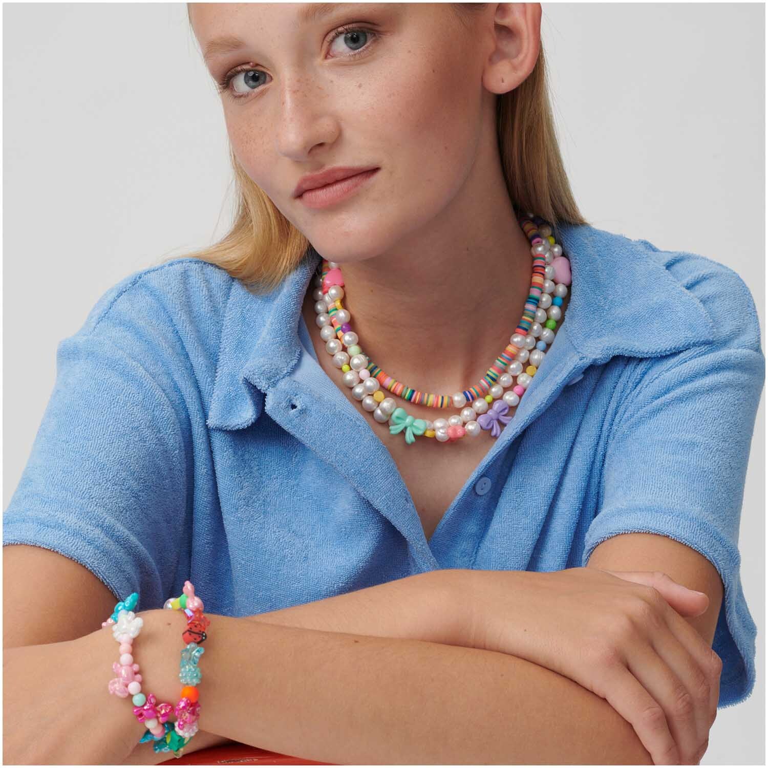 itoshii Süßwasserperlen natur, getragen von einer Frau in blauem Hemd, kombiniert mit bunten Armbändern. Ideal für stilvolle Akzente.