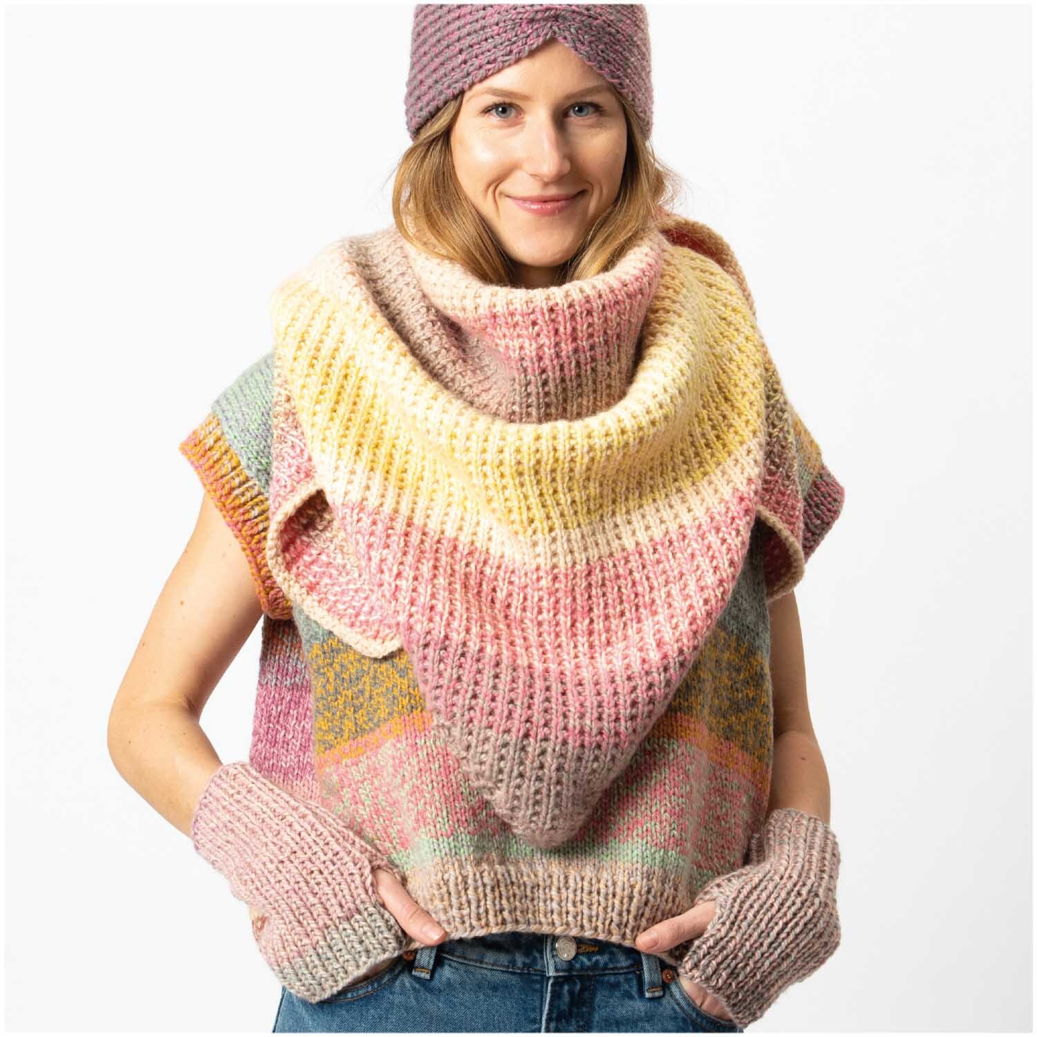 Creative Chic-Unique: Frau trägt gestricktes Set aus Schal, Mütze und Handschuhen in sanften Pastelltönen von Rico Design.