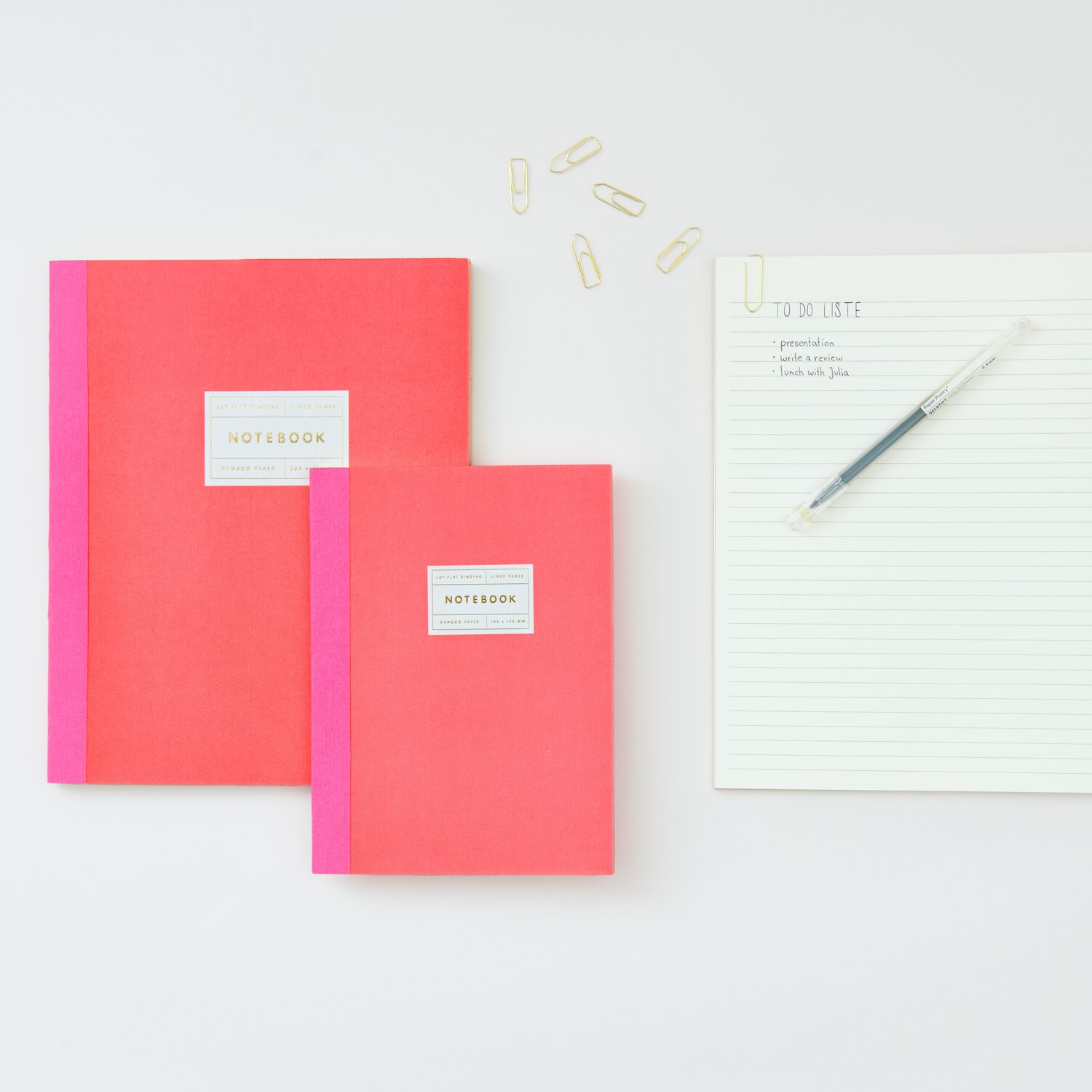 Paper Poetry Notizbuch S in Neonrot mit Goldrand von Rico Design, neben einem linierten Block und Büroklammern.