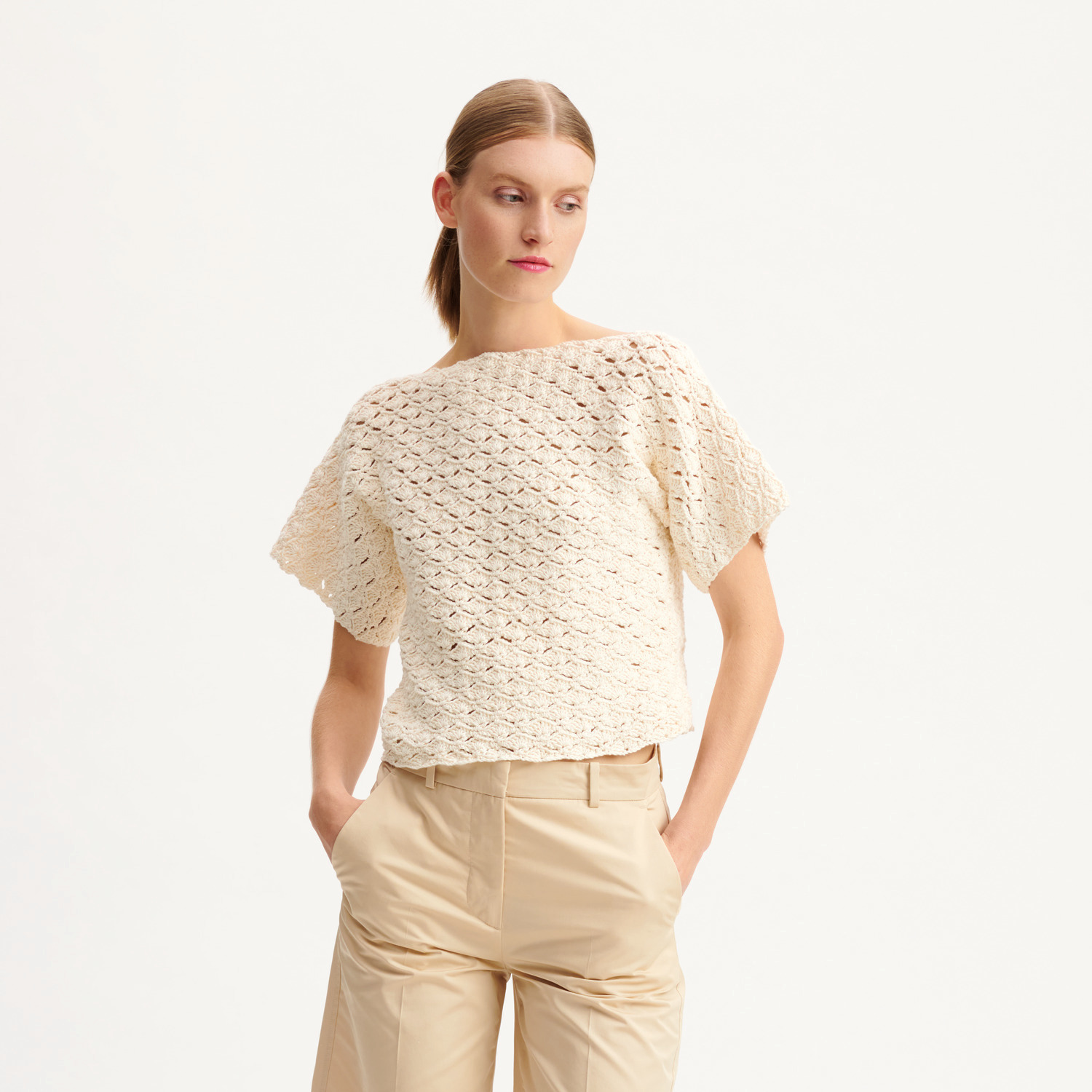 Häkelset Shirt Modell 06: Frau trägt ein cremefarbenes, gehäkeltes Shirt mit kurzen Ärmeln.