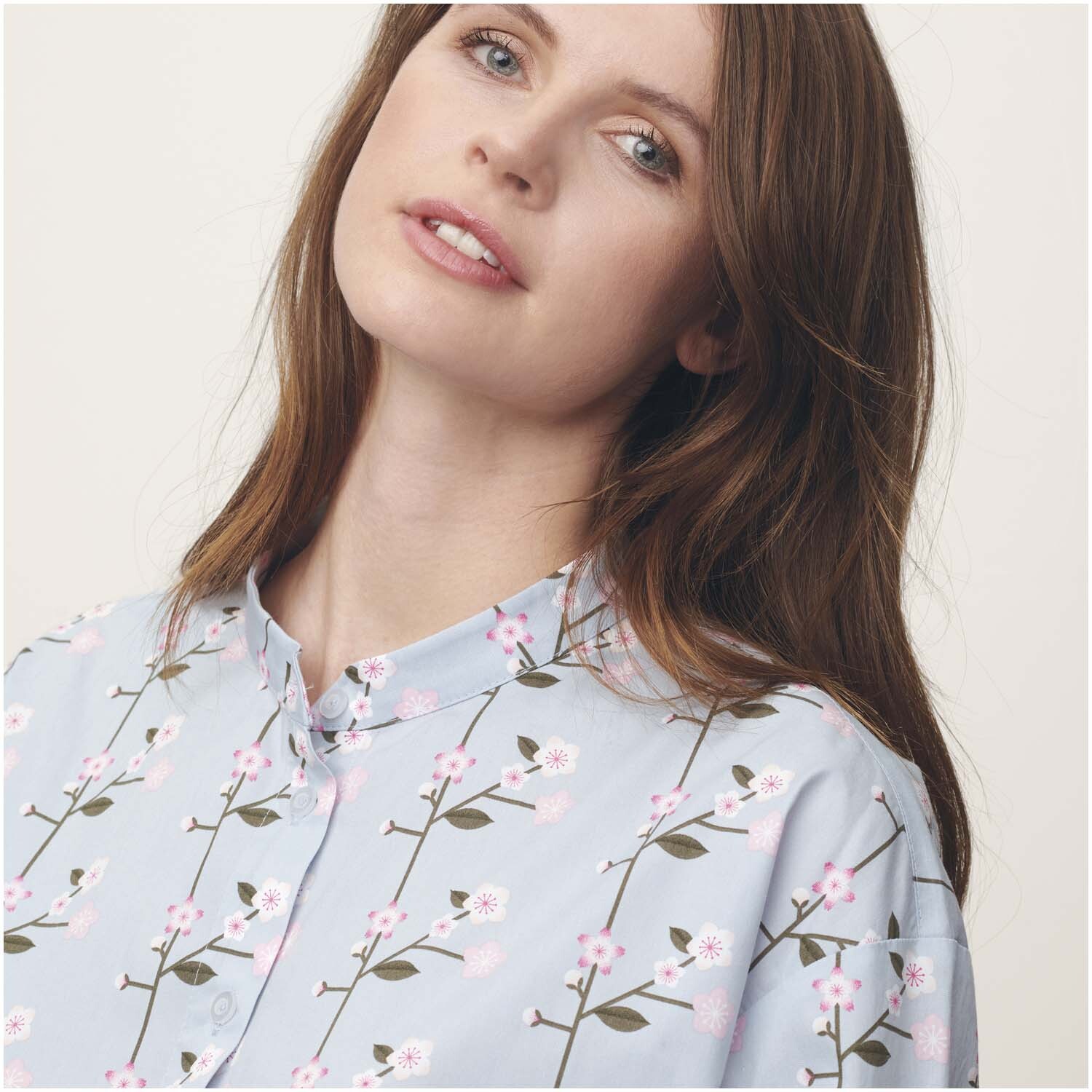 Meterware Baumwoll-Popelin mit Sakura-Zweigen auf rauchblauem Hintergrund, getragen von einer Frau. Ideal für stilvolle Nähprojekte.