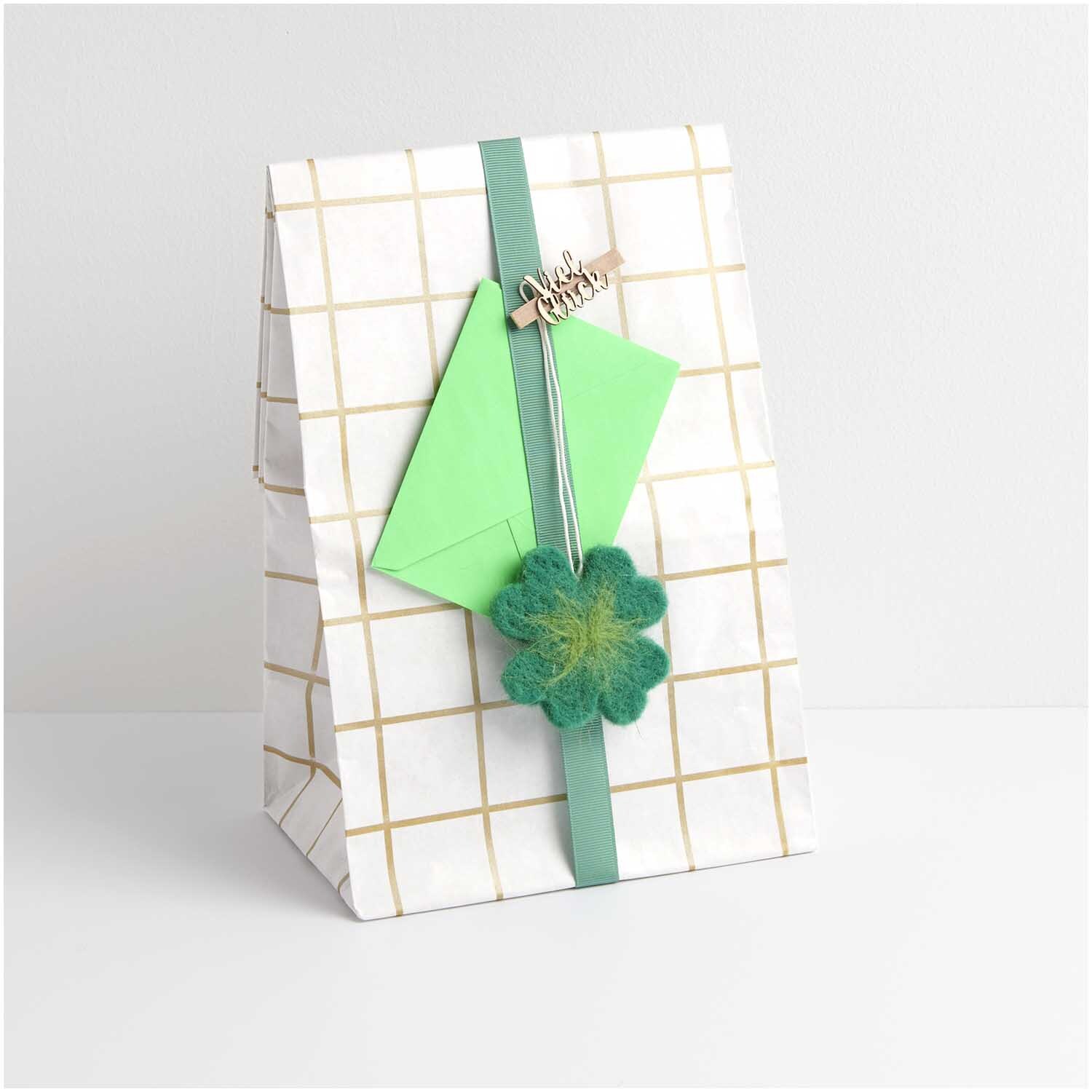 Holzklammern "Viel Glück" an einer Geschenkverpackung mit grünem Band und Filzblume von Rico Design.