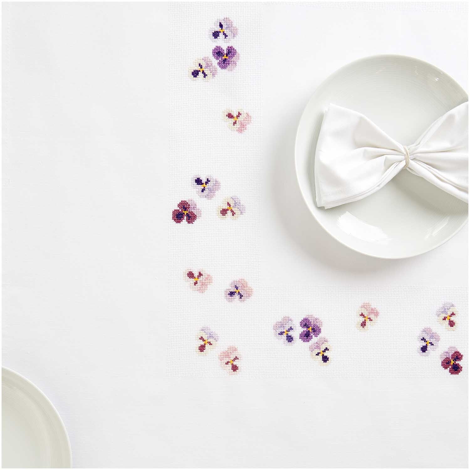 Stickpackung Tischdecke Stiefmütterchen von Rico Design zeigt zarte Blumenstickereien auf weißem Stoff, ideal für elegante Tischdekorationen.