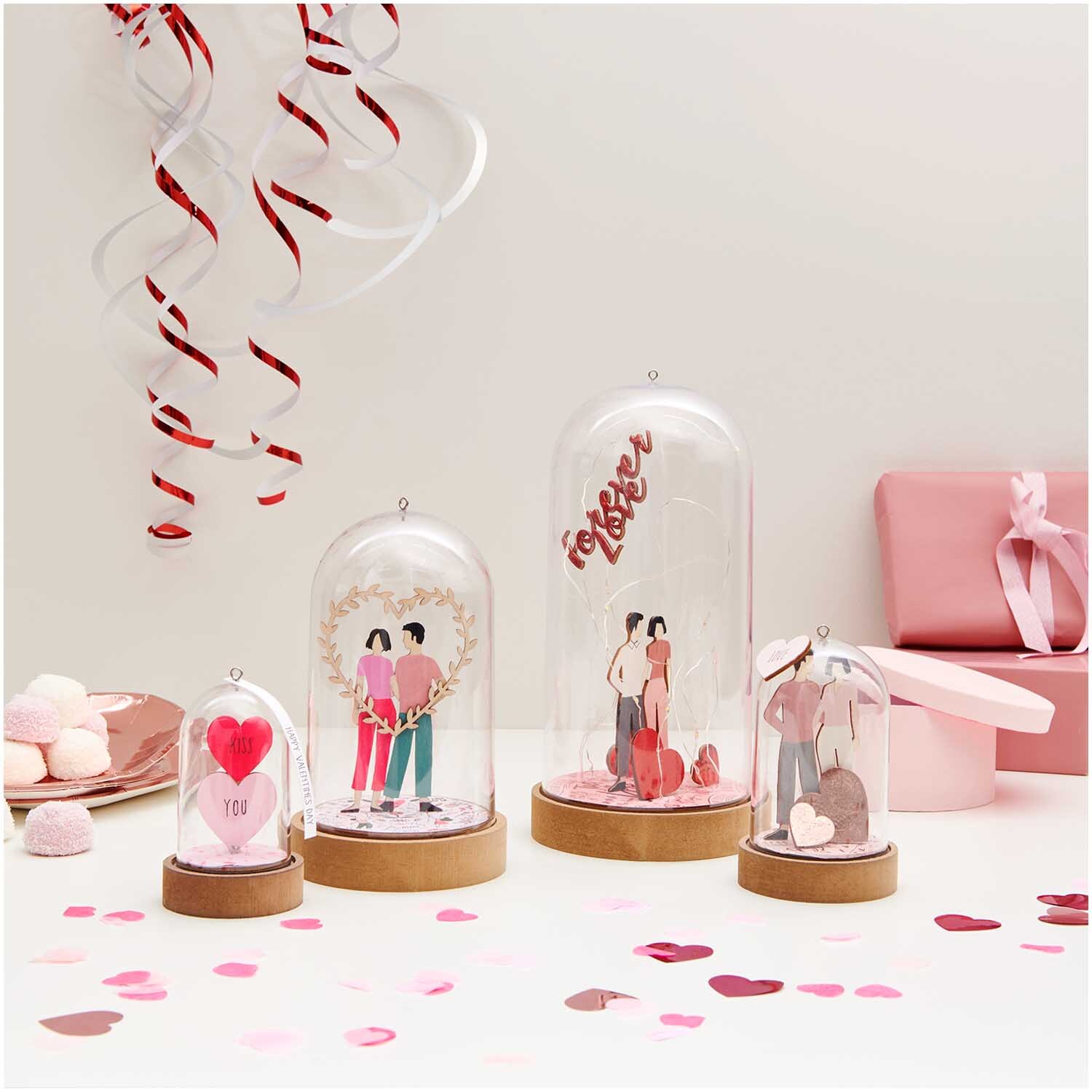 Dekohaube mit Sockel 5,5x11cm Gr. S zeigt romantische Szenen unter Glas, umgeben von rosa Geschenken und Dekorationen. Ideal für Valentinstag.