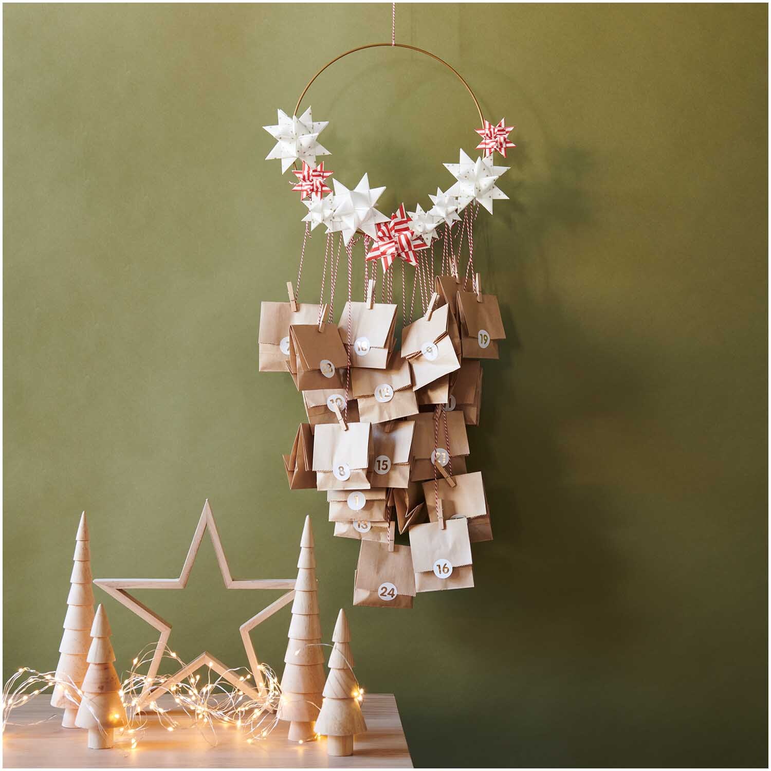 Paper Poetry Fröbelstreifen rot-weiß 60 Stück, dekorativ als Adventskalender mit Sternen und Tüten an einem Ring arrangiert, vor grünem Hintergrund.