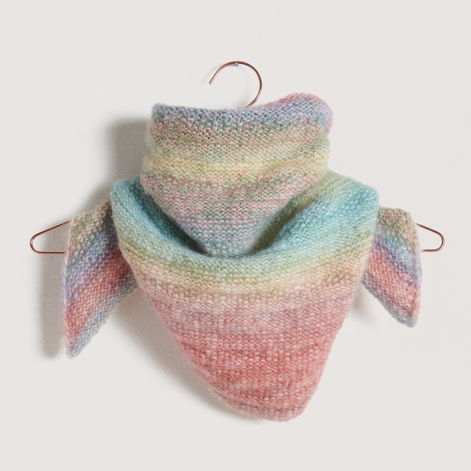 Strickset Dreieckstuch Modell 15: Weiches, pastellfarbenes Tuch in Rosa, Blau und Grün auf einem Kleiderbügel.