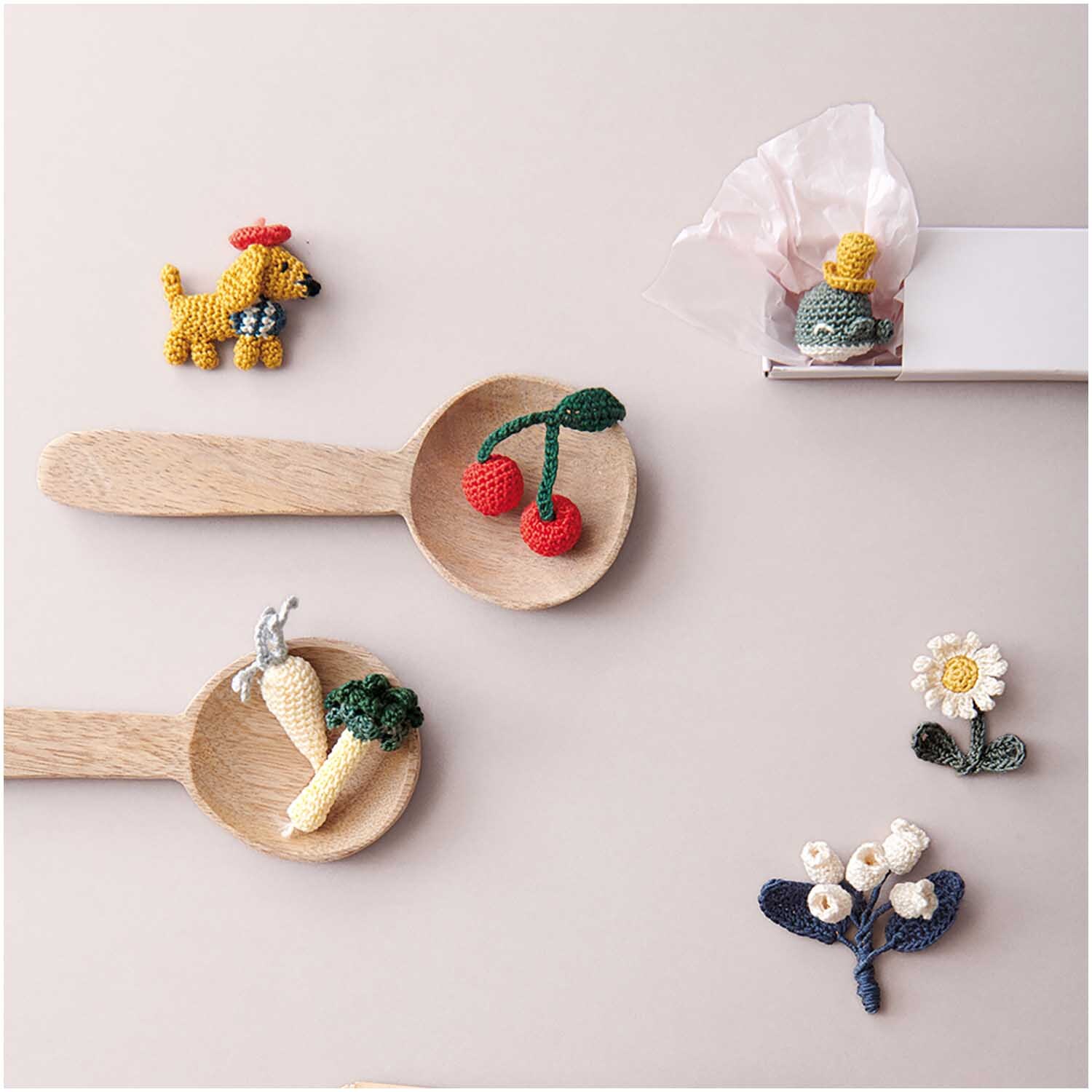 Essentials Crochet: Gehäkelte Früchte und Blumen auf Holzlöffeln, dekoriert mit einem Hund und Geschenkbox.