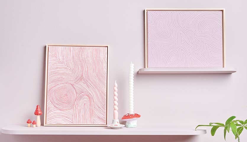 Home Acrylic: Zwei hellrosa gerahmte Kunstwerke auf weißen Regalen, dekoriert mit Kerzen und Pflanzen.