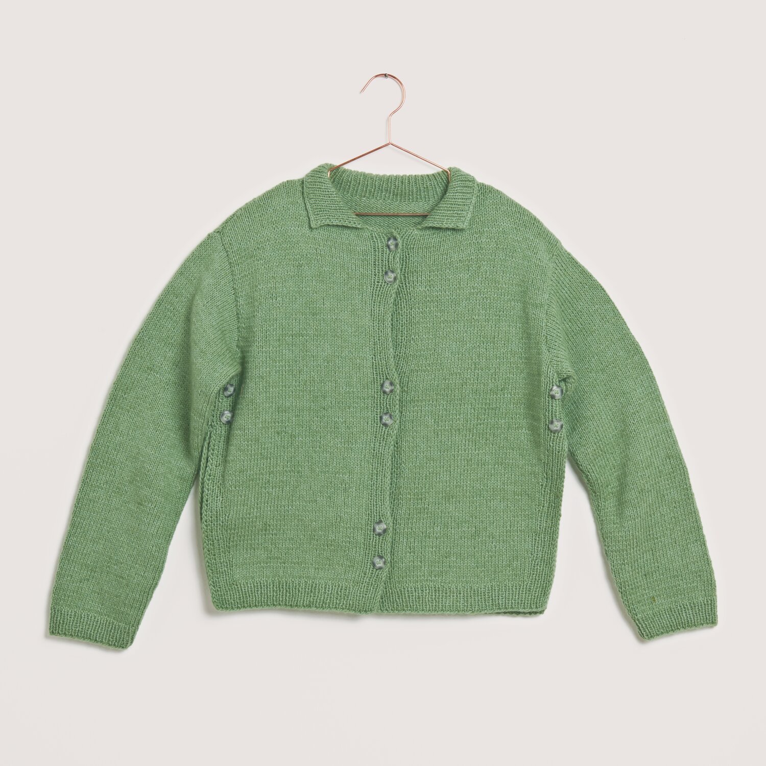 Made by Me No. 22 Frühjahr-Sommer: Grüner Strickcardigan aus Creative Cotton Fleece dk, präsentiert auf einem Kleiderbügel.