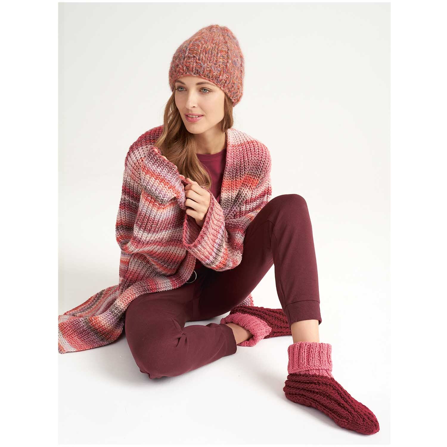 Rustikal Hauswolle: Frau in gestricktem Outfit mit Mütze und Socken in Rosa, Marke Wolle Rödel.