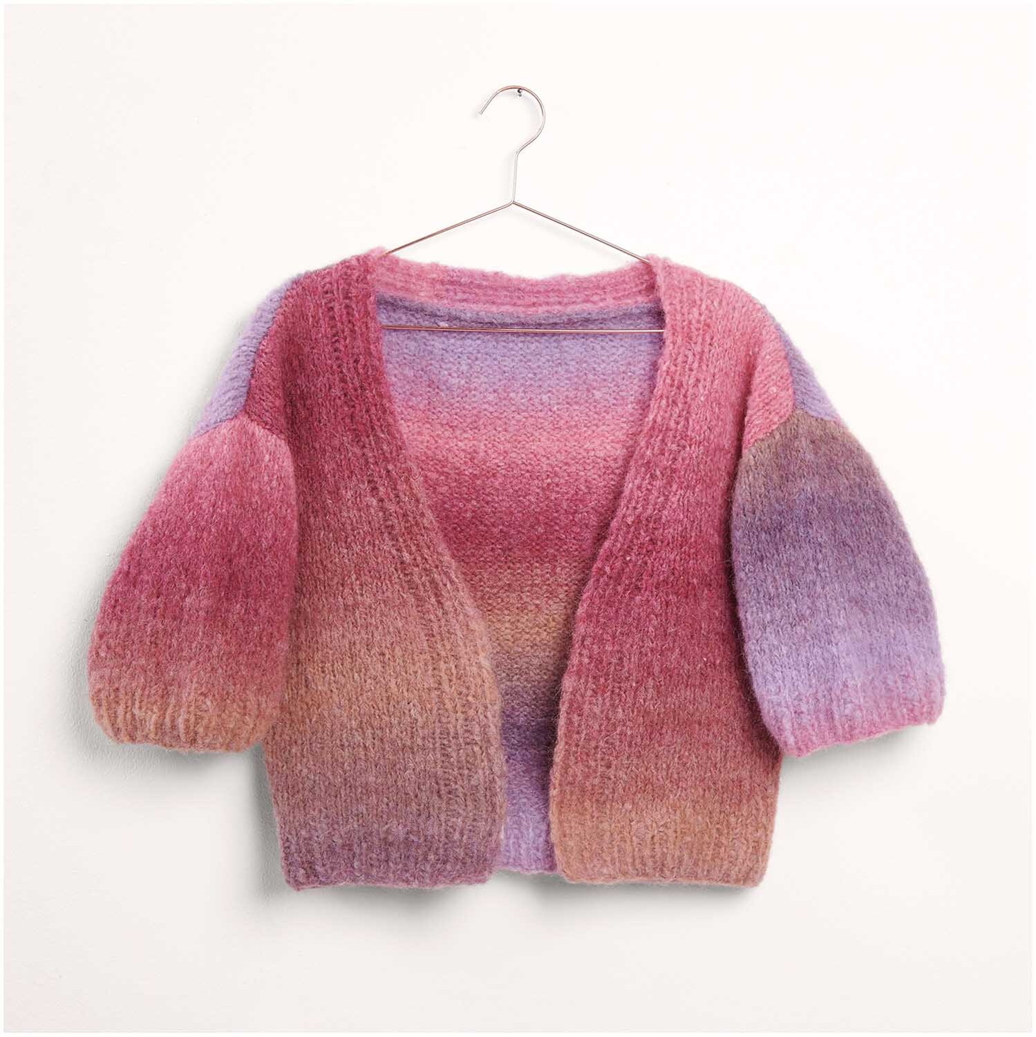 Strickset Kimonojacke Modell 01: Bunte, gestrickte Jacke mit Farbverlauf von Rosa zu Lila, hängend an einem Kleiderbügel.