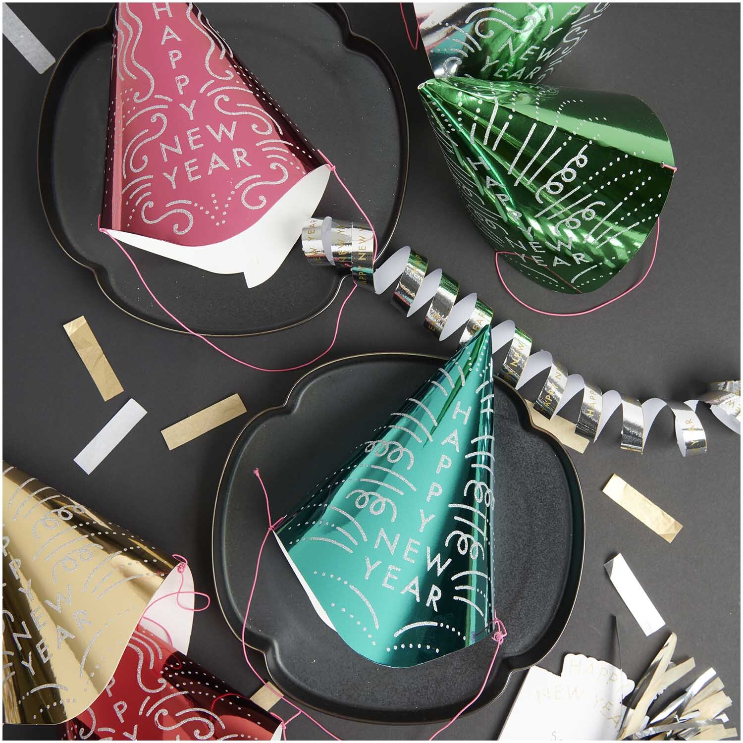 Paper Poetry Partyhüte in verschiedenen Farben auf einem Tisch mit Dekorationen für Silvester.