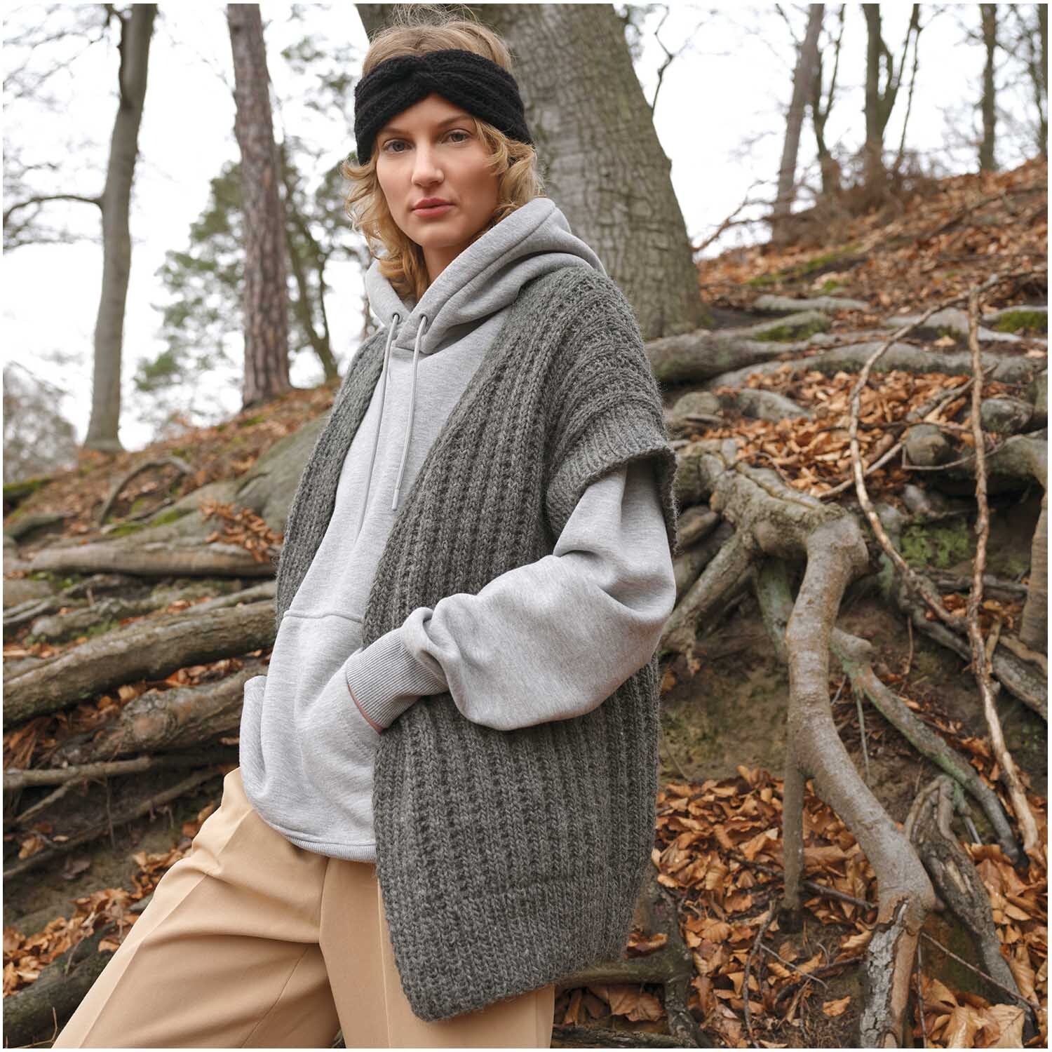 Strickset Stirnband Modell 12: Frau im Wald mit grauem Strickcardigan und schwarzem Stirnband.
