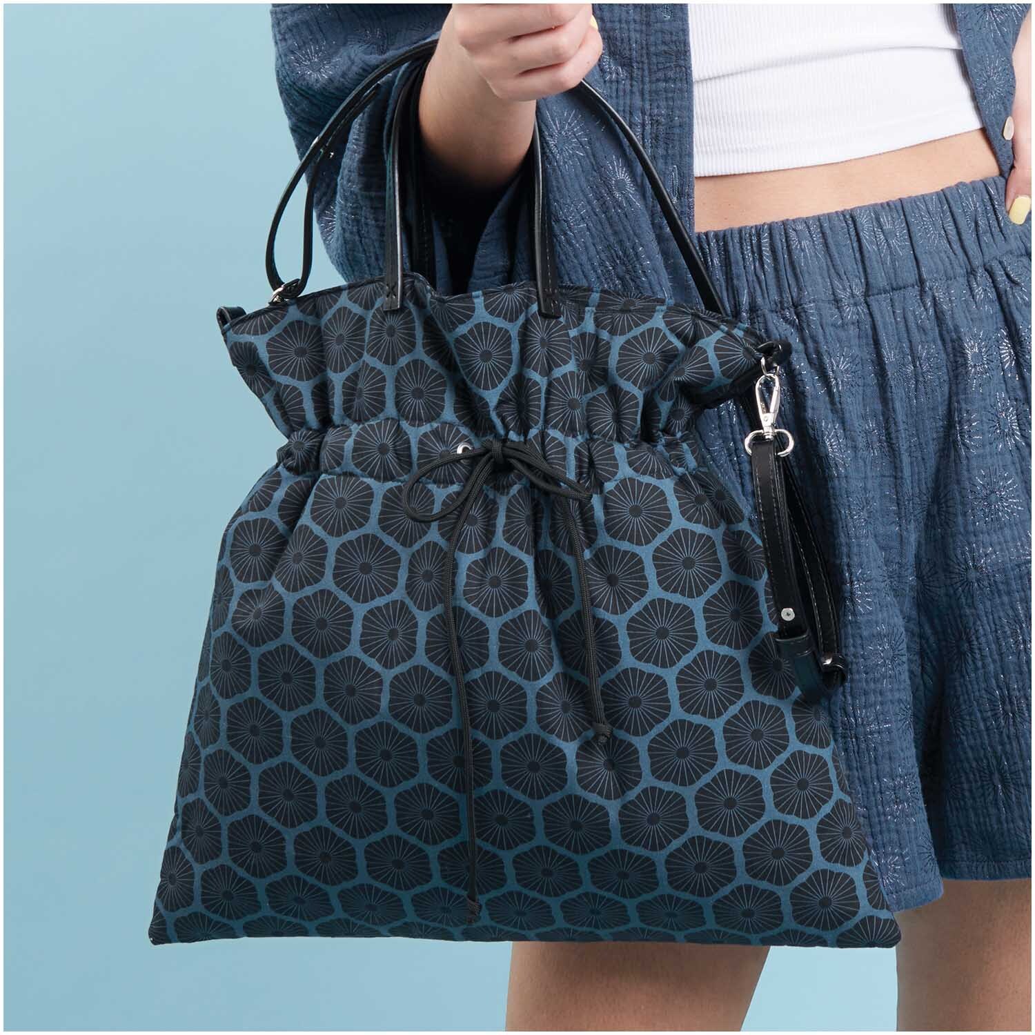 Meterware Baumwoll-Popelin blau Rosette: Frau trägt eine stilvolle Tasche mit blauem Rosettenmuster von Rico Design.