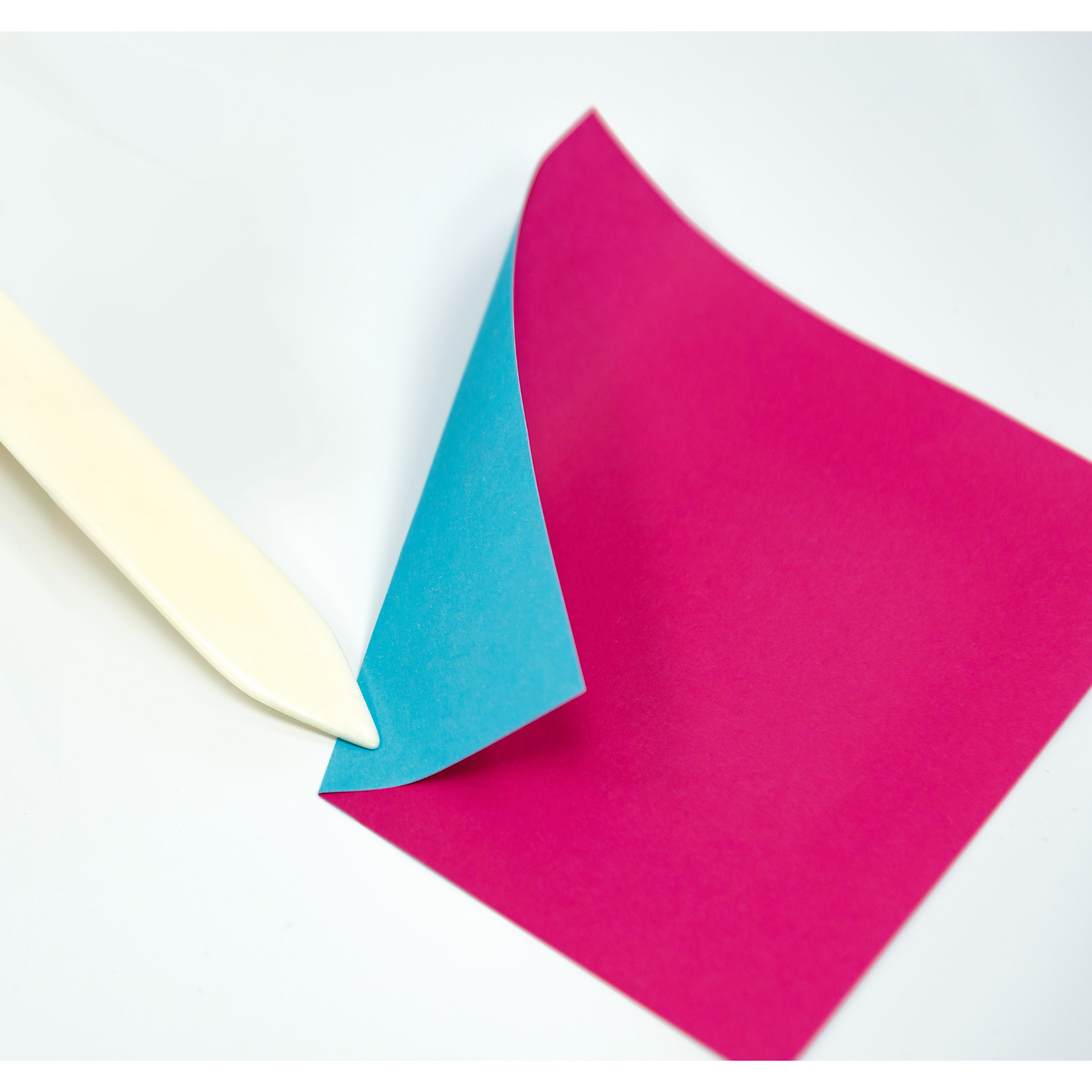 Falzbein aus Knochen, ideal zum Falten von Papier. Gezeigt mit pink-blauem Papier, Größe 15x2cm.