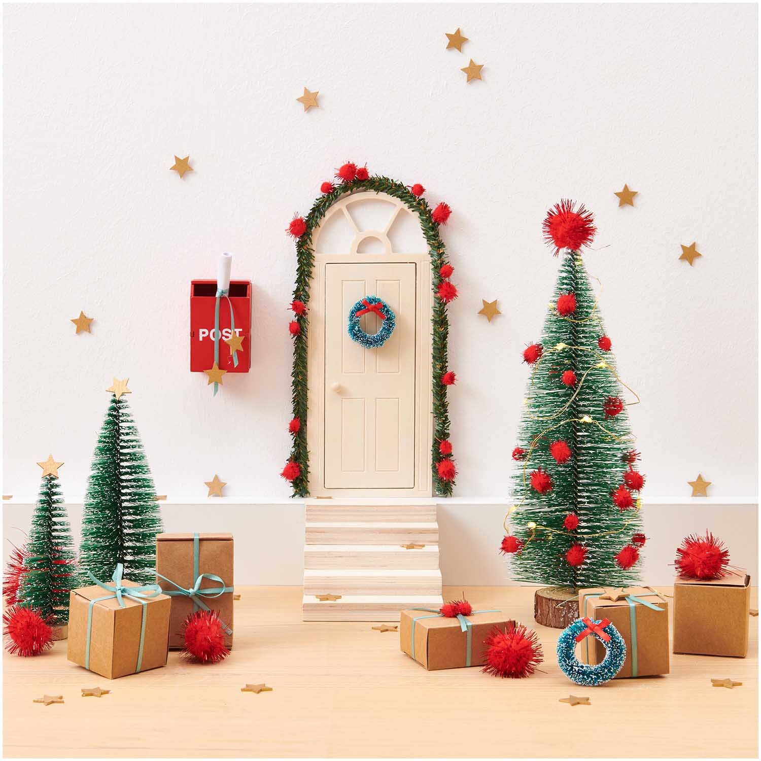 Miniatur Geschenkschachteln 6 Stück von Rico Design vor einer festlichen Weihnachtsszene mit dekorierten Bäumen und Tür.