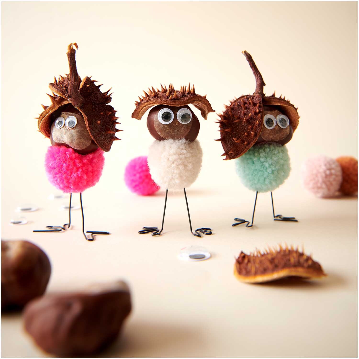 Garn Pompons 24 Stück von Rico Design in Pastell Mix, dekoriert als kreative Figuren mit Kastanienhüten und Wackelaugen auf einem hellen Hintergrund.