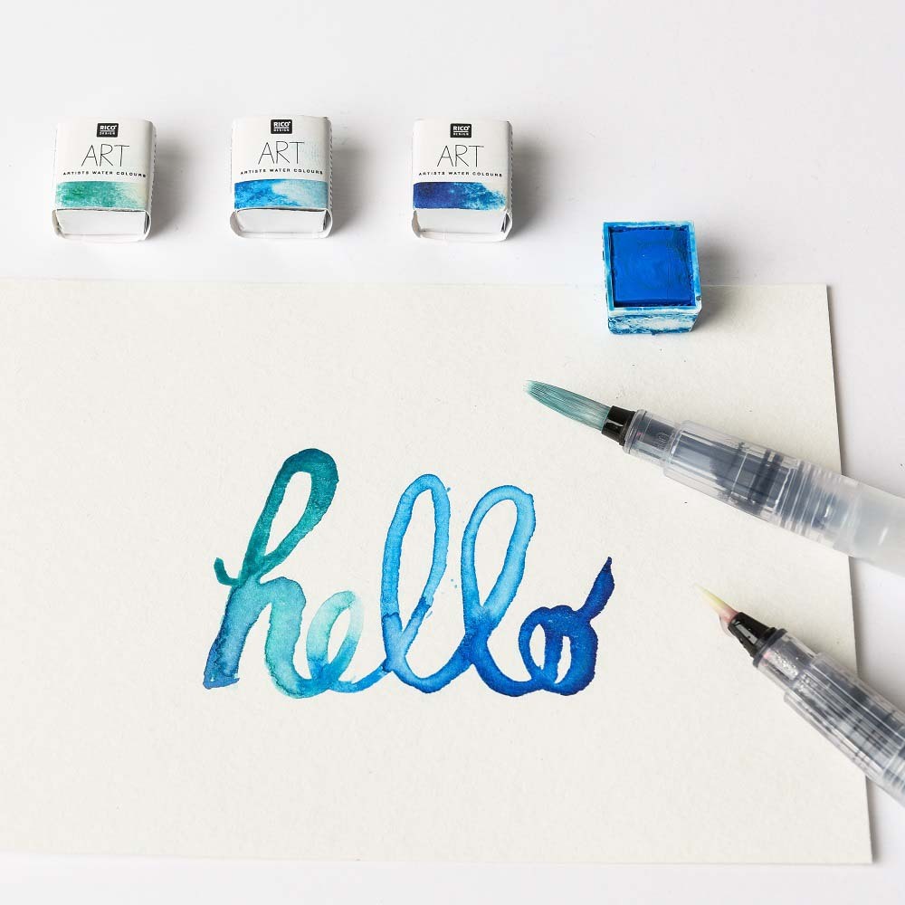 Wassertankpinselset rund von Rico Design, 3-teilig, neben Aquarellfarben und einem Blatt mit "hello".