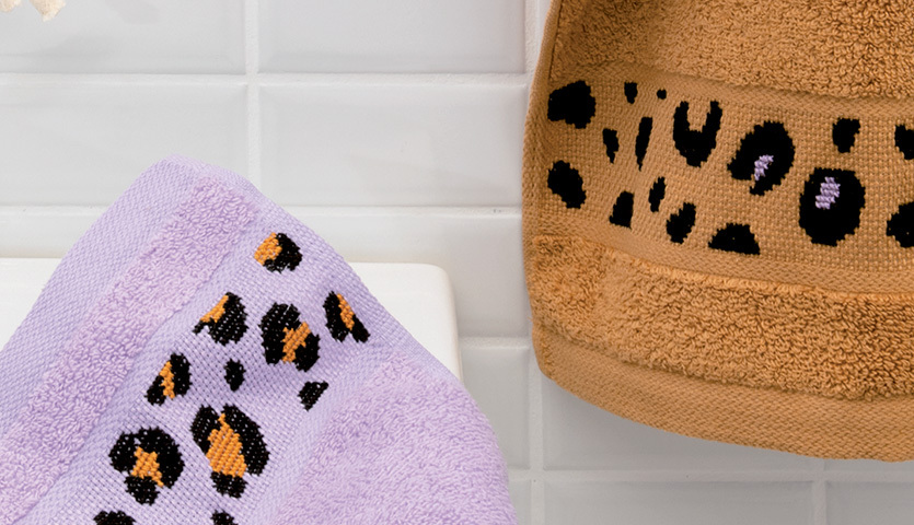Stickanleitung Handtuch im Leo-Design: Zwei Handtücher mit Leopardenmuster in Lila und Braun auf weißem Hintergrund.
