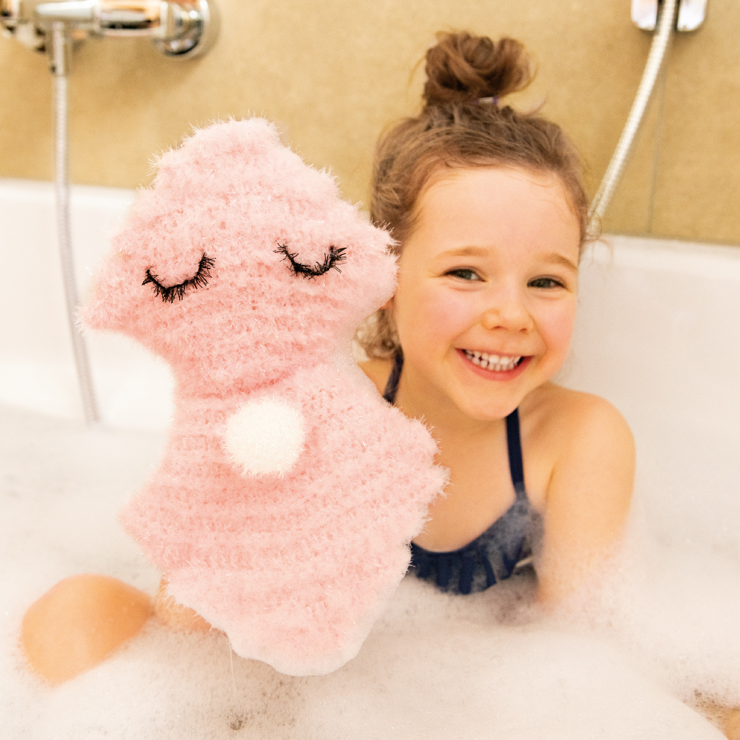 Häkelanleitung Waschhandschuh Muschel: Ein Kind hält einen rosa Waschhandschuh in Muschelform in einer Badewanne.