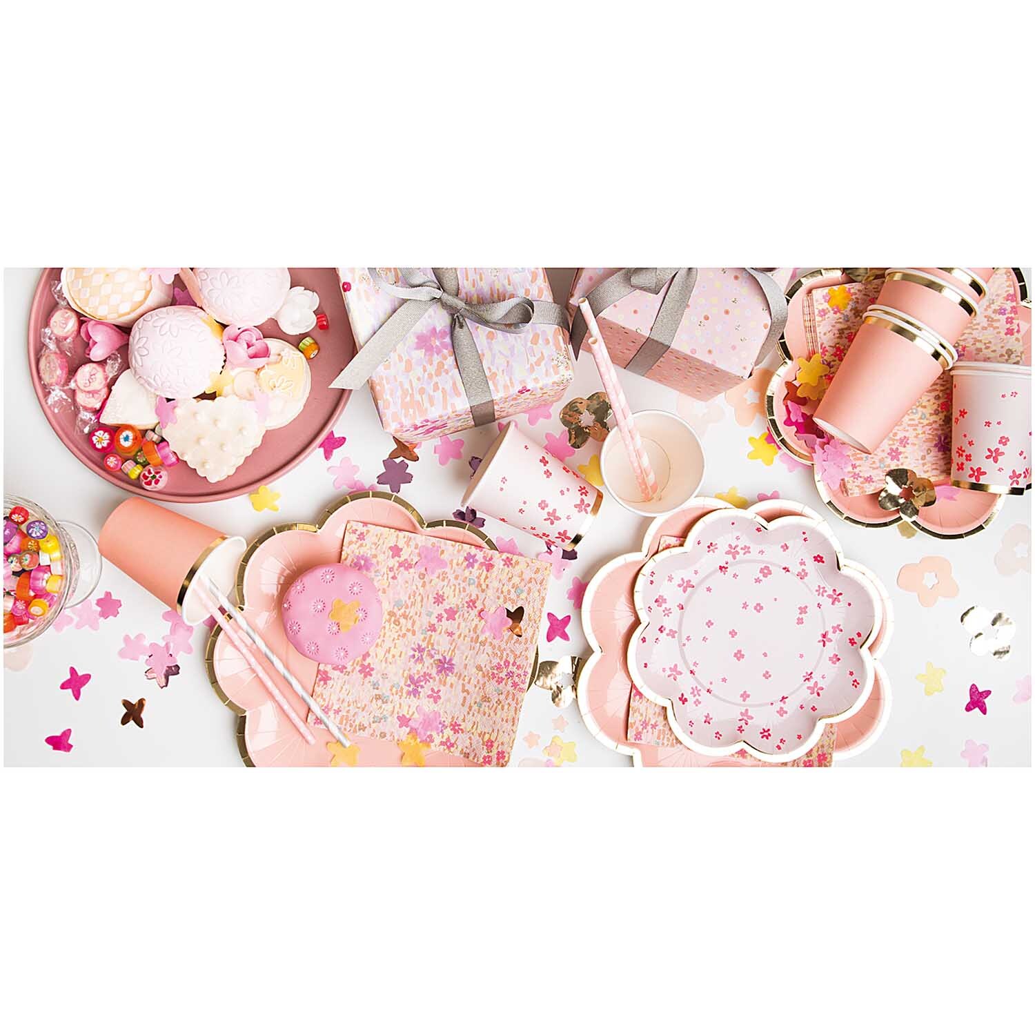 Pappteller Blume Blüten rosa 21cm 12 Stück, dekoriert mit Partyzubehör und Süßigkeiten auf einem Tisch.