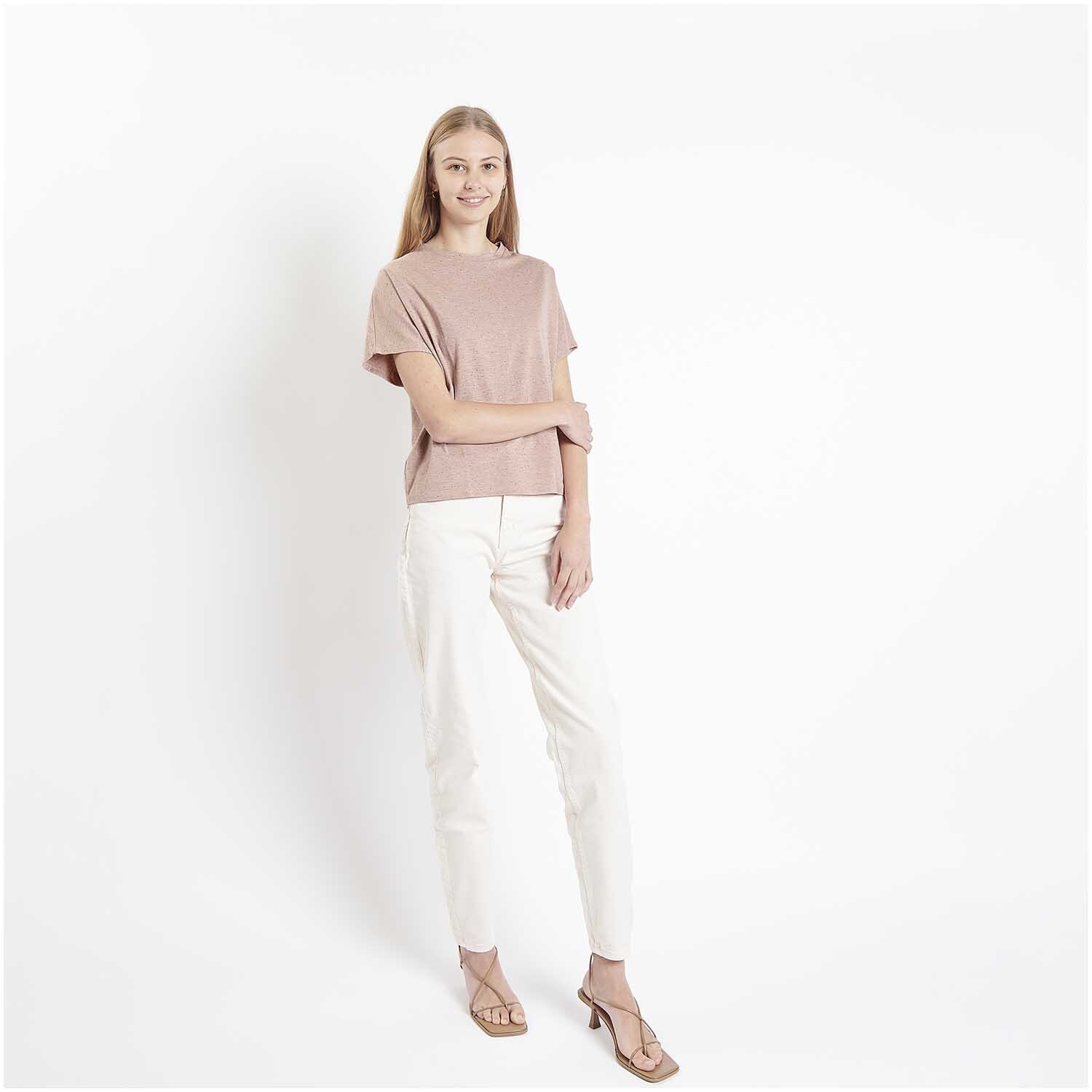 Meterware Jersey Flocken Puder: Frau in puderfarbenem Rico Design Oberteil und weißer Hose, stehend vor weißem Hintergrund.