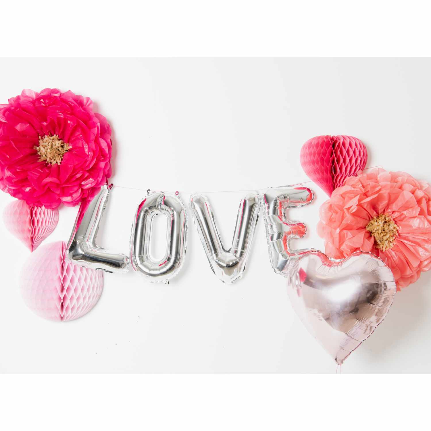Folienballon Buchstabe silber 36cm: Silberne Ballons formen das Wort "LOVE", umgeben von rosa und roten Papierblumen.