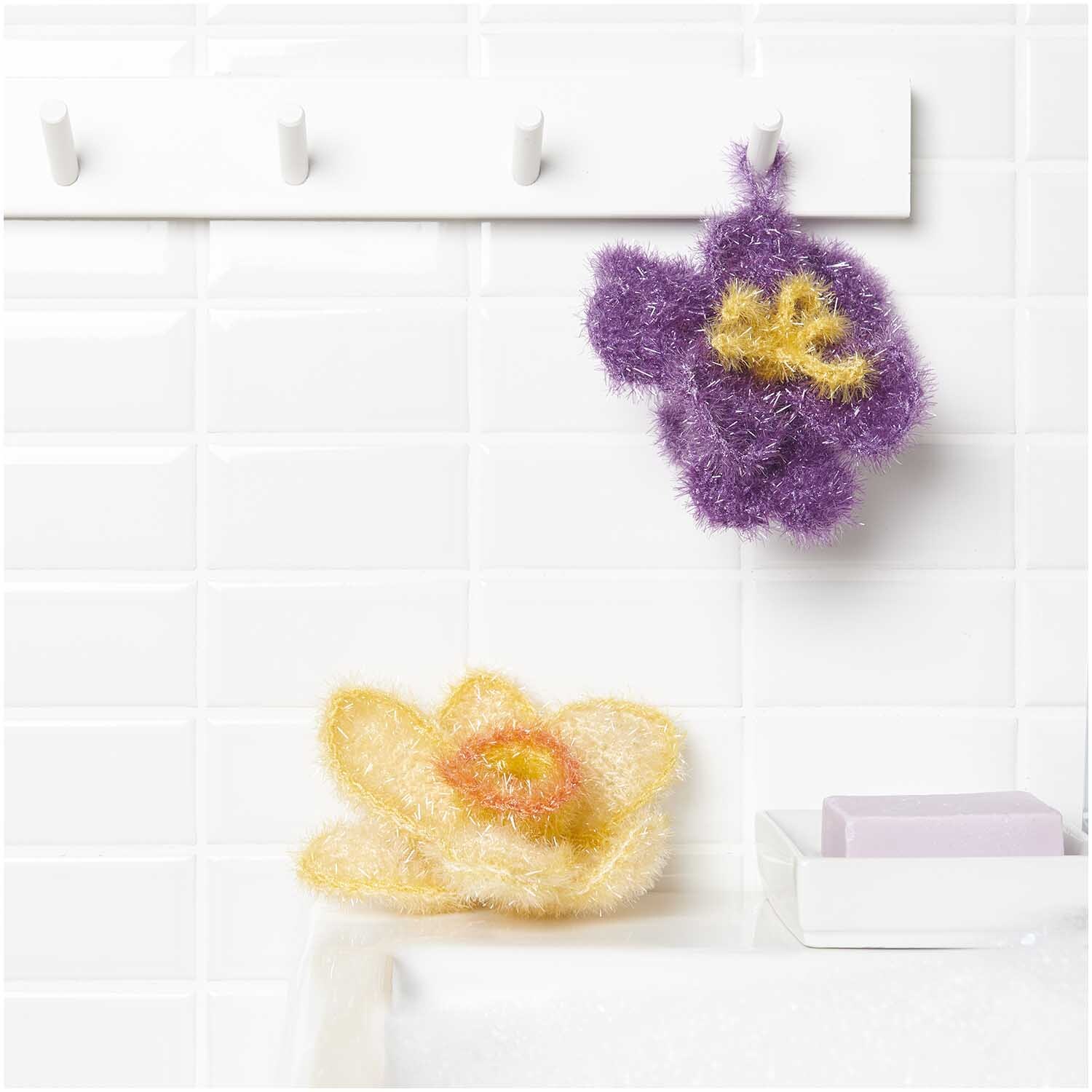 Häkelset Creative Bubble Frühlingsblume: Zwei gehäkelte Blumen in Lila und Gelb von Rico Design, dekorativ im Badezimmer platziert.