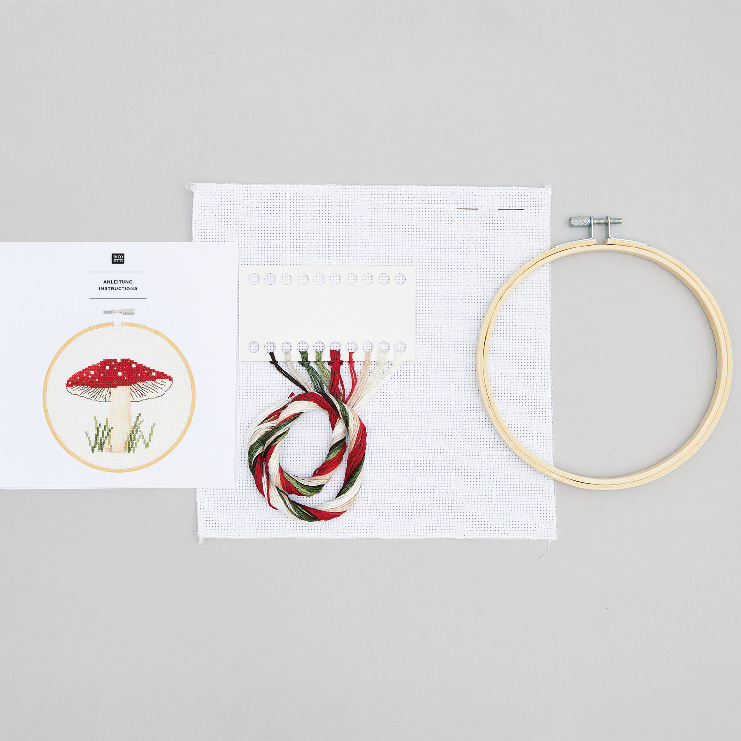 Stickpackung Shrooom Pilz von Rico Design zeigt Stickrahmen, Garn und Vorlage auf grauem Hintergrund. Ideal für kreative Handarbeiten.