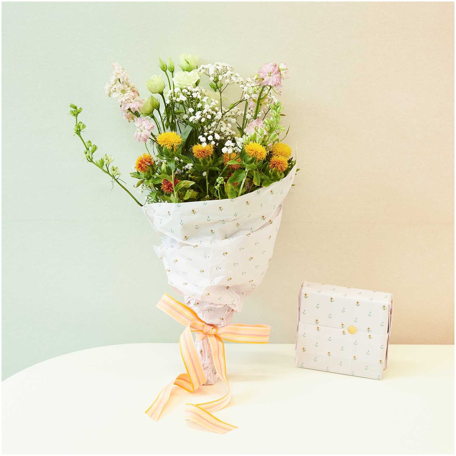 Seidenpapier Pixel Blumen umhüllt einen bunten Blumenstrauß, daneben eine passende Geschenkbox.