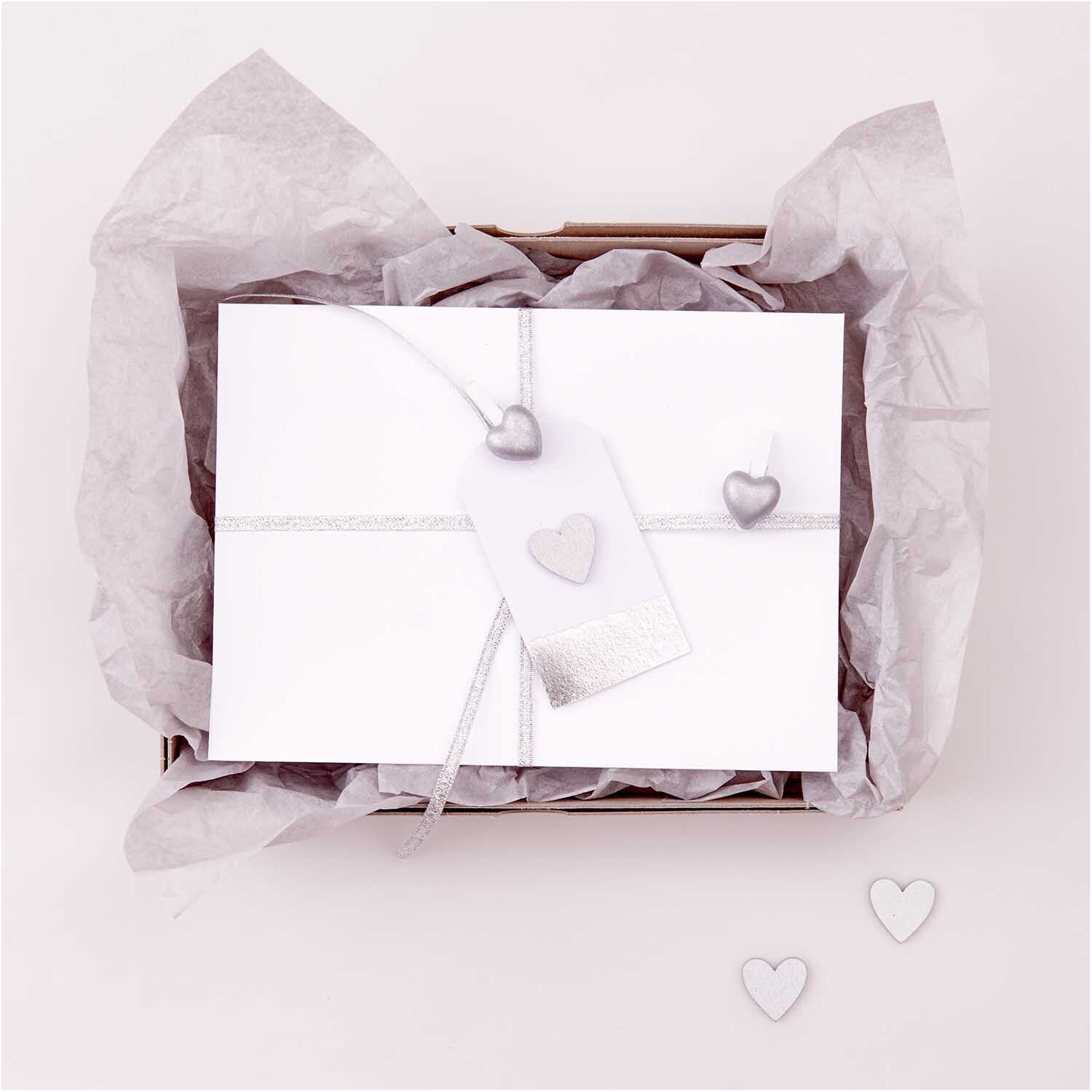 Holzstreu Herz 48 Stück: Elegante silberne Herzen von Rico Design auf weißem Geschenkpapier.